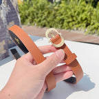 Orange leather belt held up, showing gold-tone buckle and metal prong