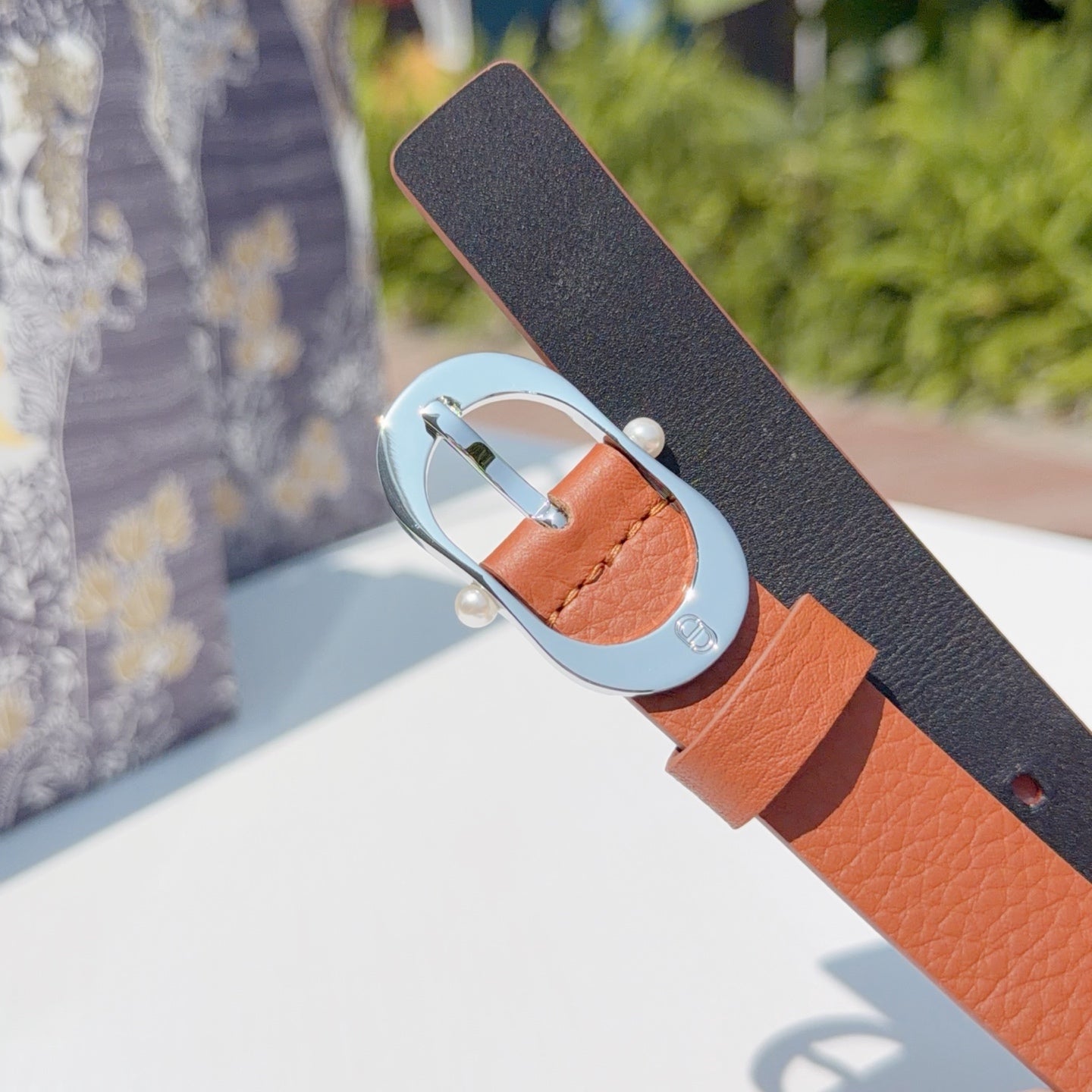 Leather belt with dark underside strap and orange top, round silver buckle