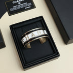 Gold-tone cuff bracelet with CHANEL lettering, shown in a black gift box