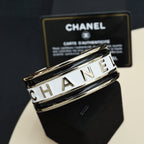 Gold-tone cuff bracelet with white CHANEL lettering on the stacked bands