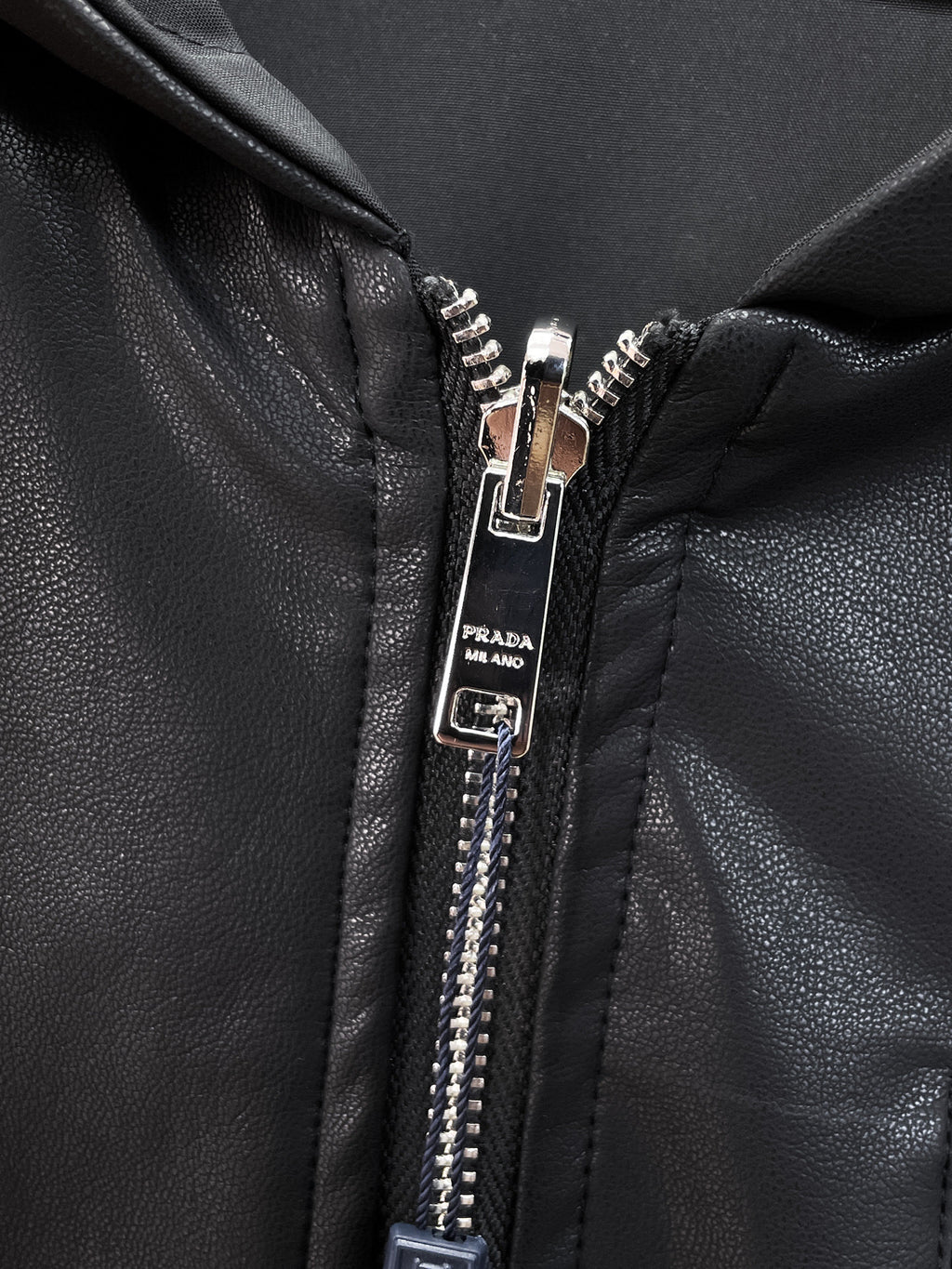 Dark jacket zipper pull with Prada logo label and silver teeth