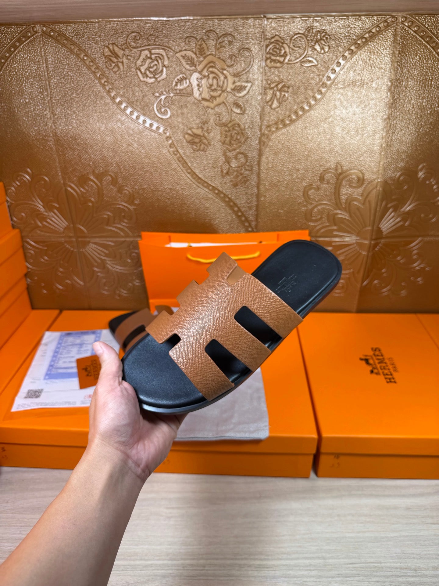 Brown and black slide sandals held in hand, showing wide strap cutouts