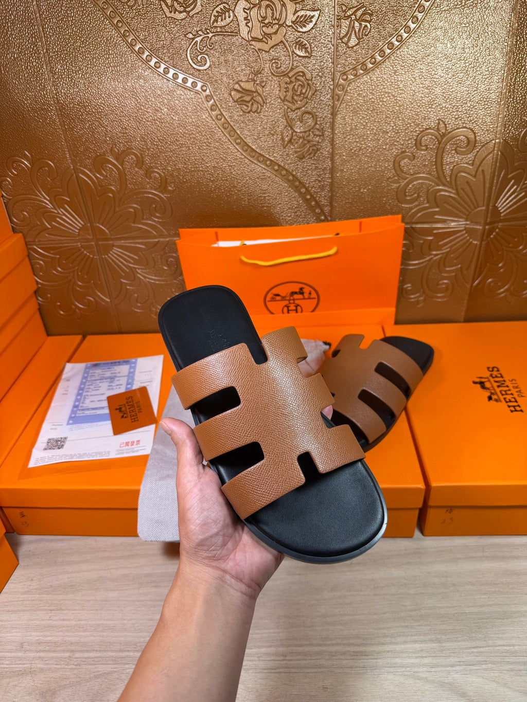 Brown-and-black slide sandals with wide straps and dark footbeds, held up