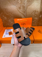 Brown-and-black slide sandals with wide straps and dark footbeds, held up