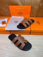 Brown and black slide sandals with wide straps and dark footbed, shown on boxes