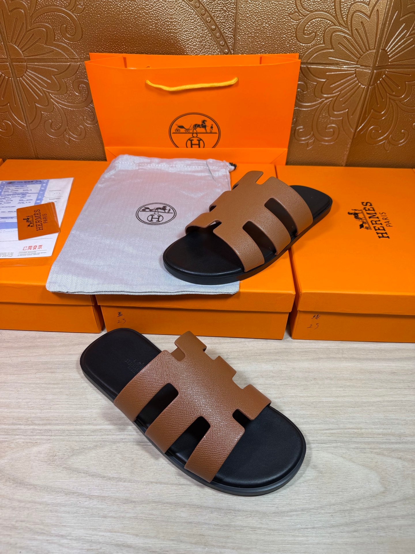 Brown and black slide sandals with wide straps and dark footbed, shown on boxes