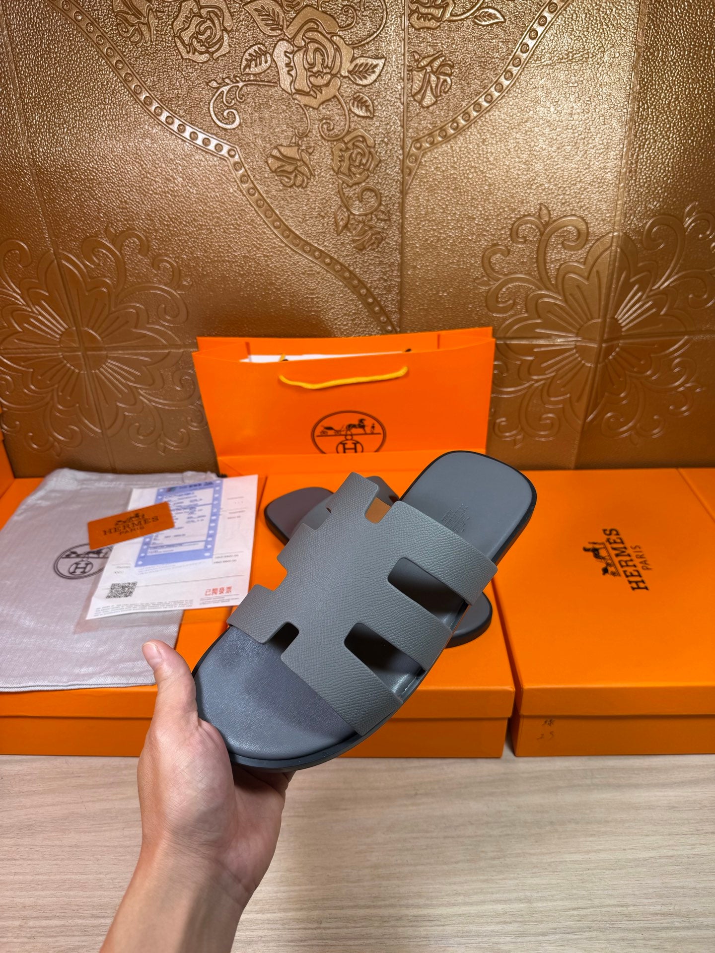 Hermes slide sandals in dark blue held in hand, open toe with cutout straps