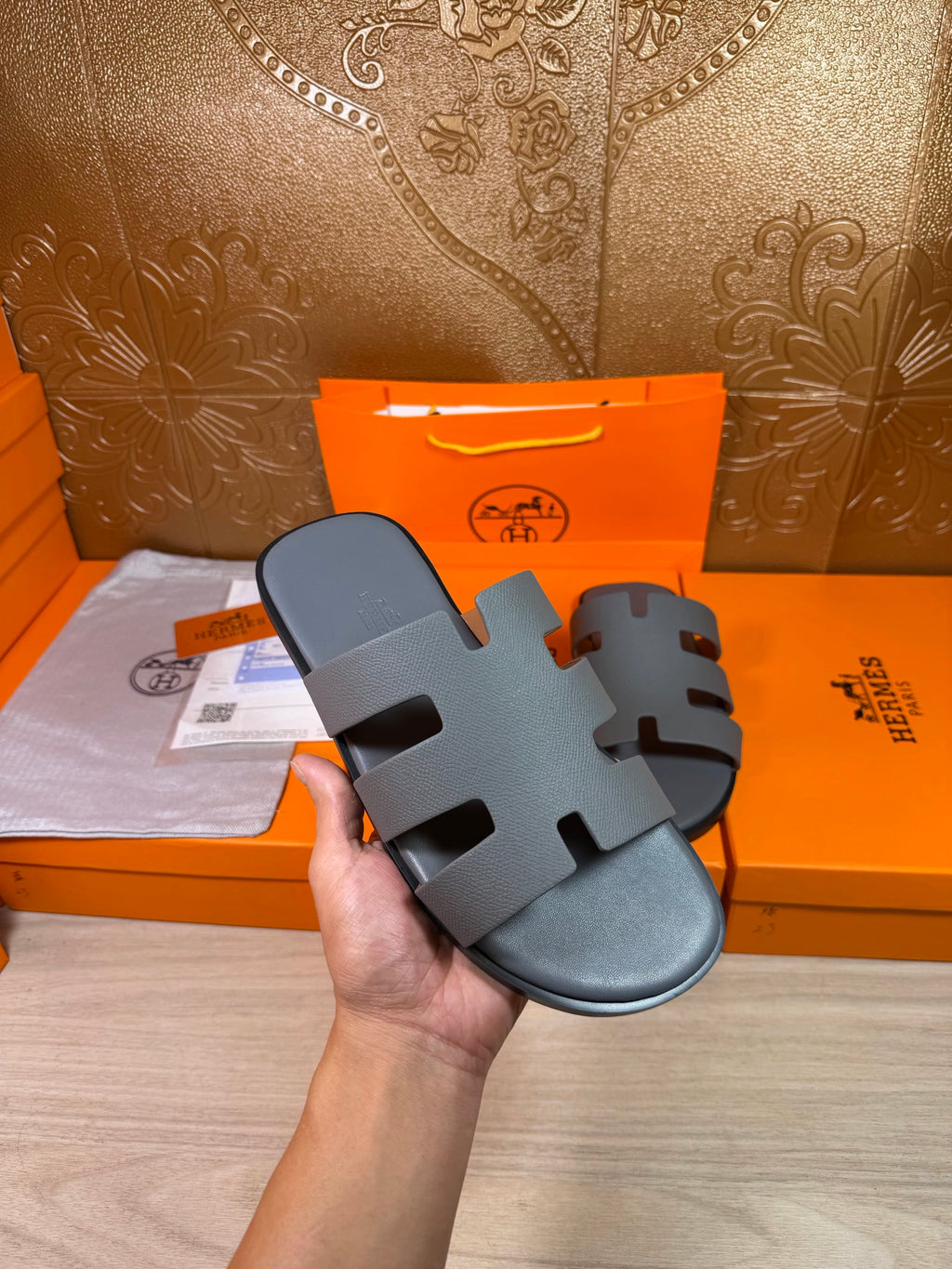 Hermes slide sandal in dark blue held in hand, showing wide cutout strap