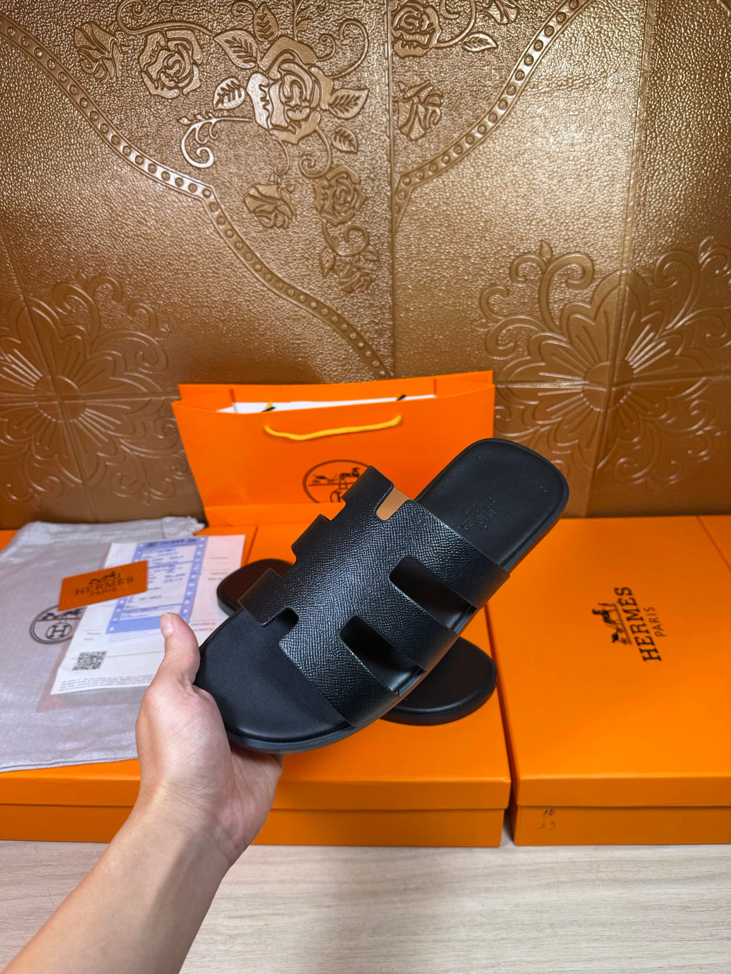Black slide sandals with wide strap band and open toe, held above the pair