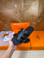 Black slide sandals with wide strap band and open toe, held above the pair