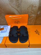 Black slide sandals with wide strappy upper and open toe, buckle-like closure