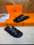 Black slide sandals with wide straps and buckle-like accents, open toe view