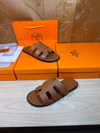 Two brown slide sandals with wide cutout straps, flat sole, and dark edge trim.