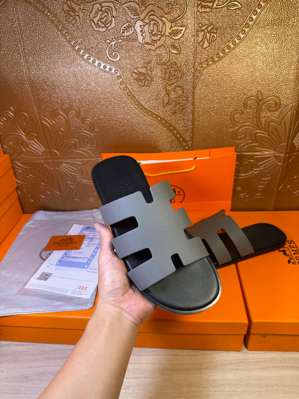 Hermes slide sandal in hand, dark footbed with light gray striped straps