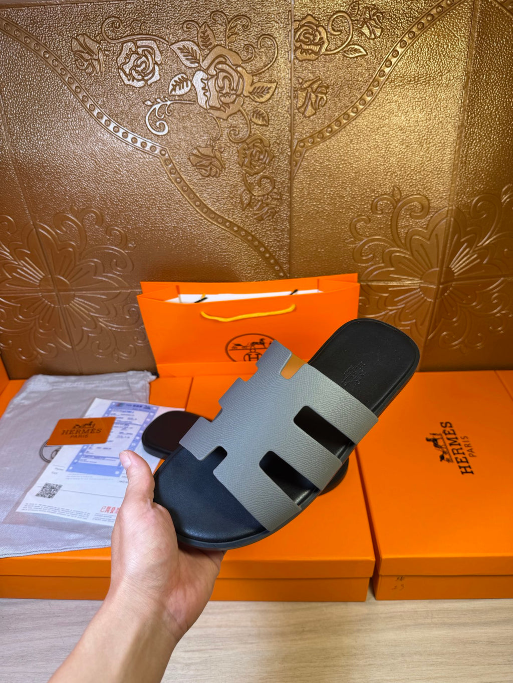 Hermes slide sandal held in hand, black footbed with light gray straps