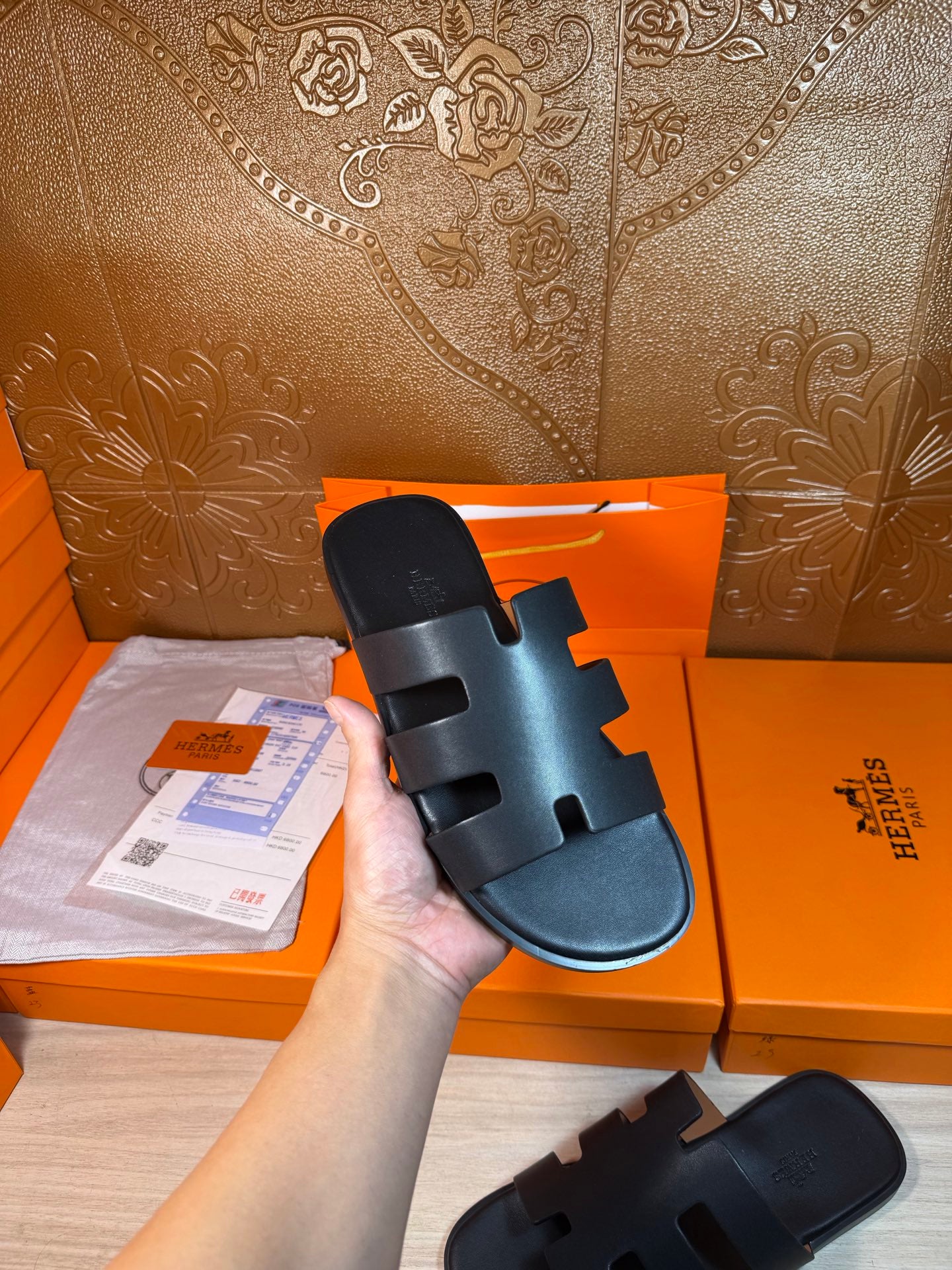 Hermes slide sandals held in hand, dark navy leather upper and open toe