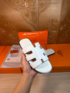 Hermes sandals held up: white multi-strap slide sandals, open toe