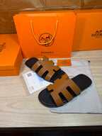 Hermes slide sandals with tan straps and black sole, front angled view.