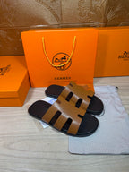 Hermes slide sandals with tan cutout straps and black sole, side view.