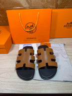 Hermes slide sandals with tan leather-style straps and black rubber sole, front view.