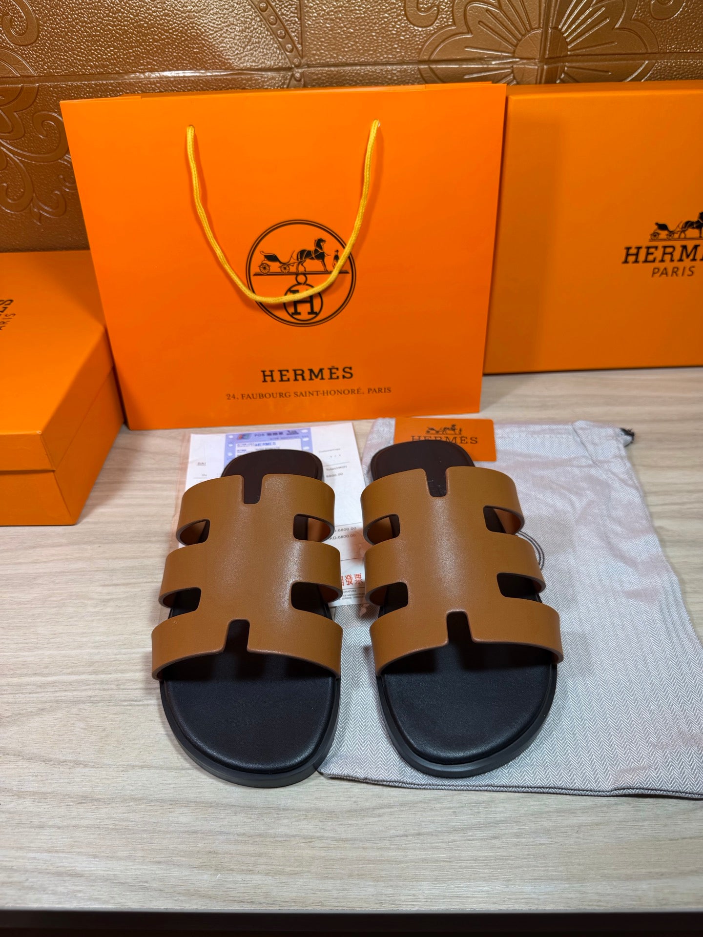 Hermes slide sandals with tan leather-style straps and black rubber sole, front view.