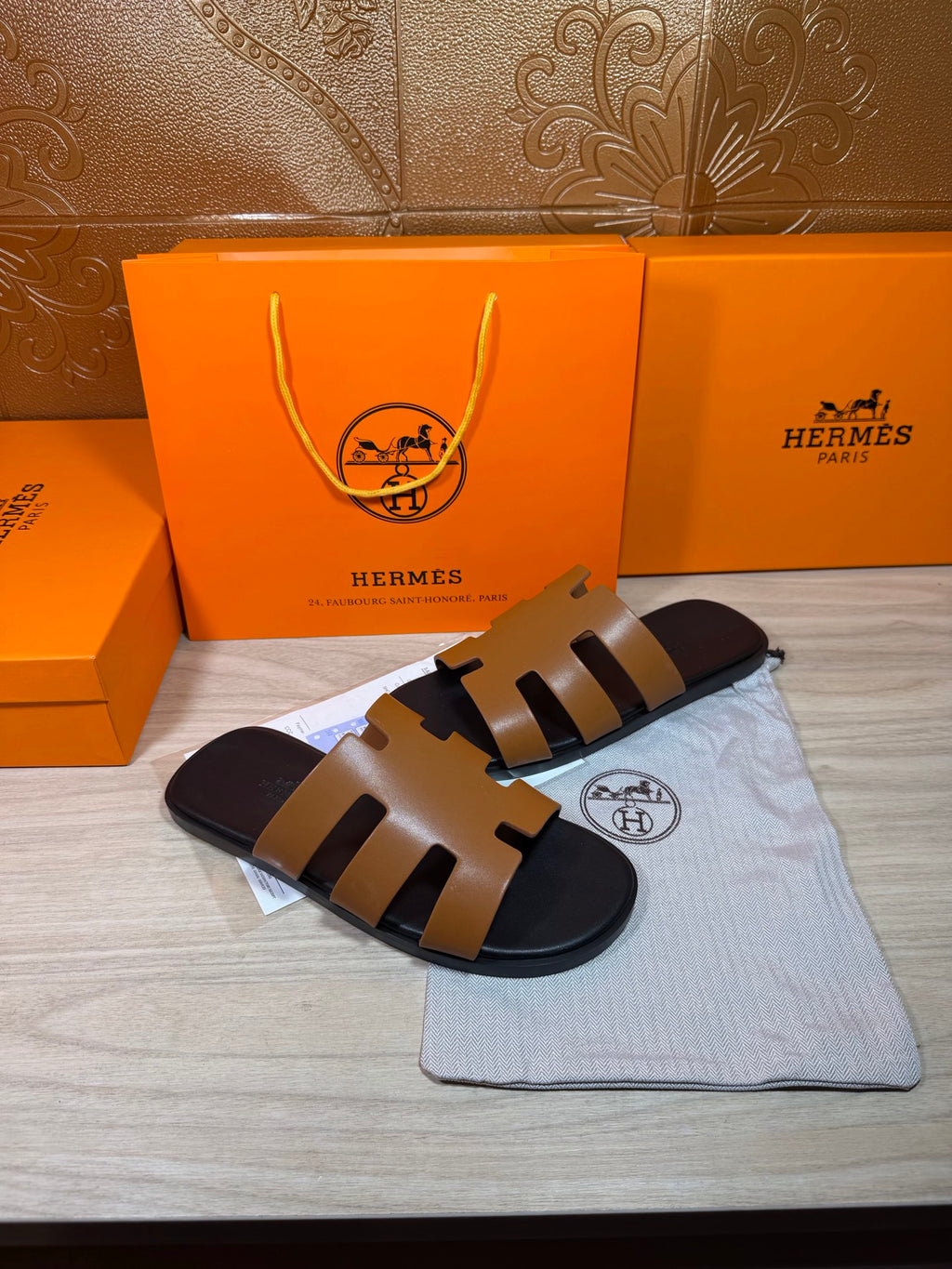 Hermes slide sandals with tan straps and black footbed, laid flat with dust bag.