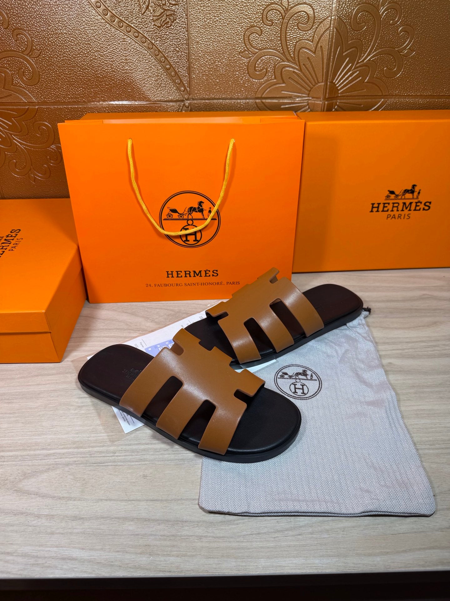Hermes slide sandals with tan straps and black footbed, laid flat with dust bag.