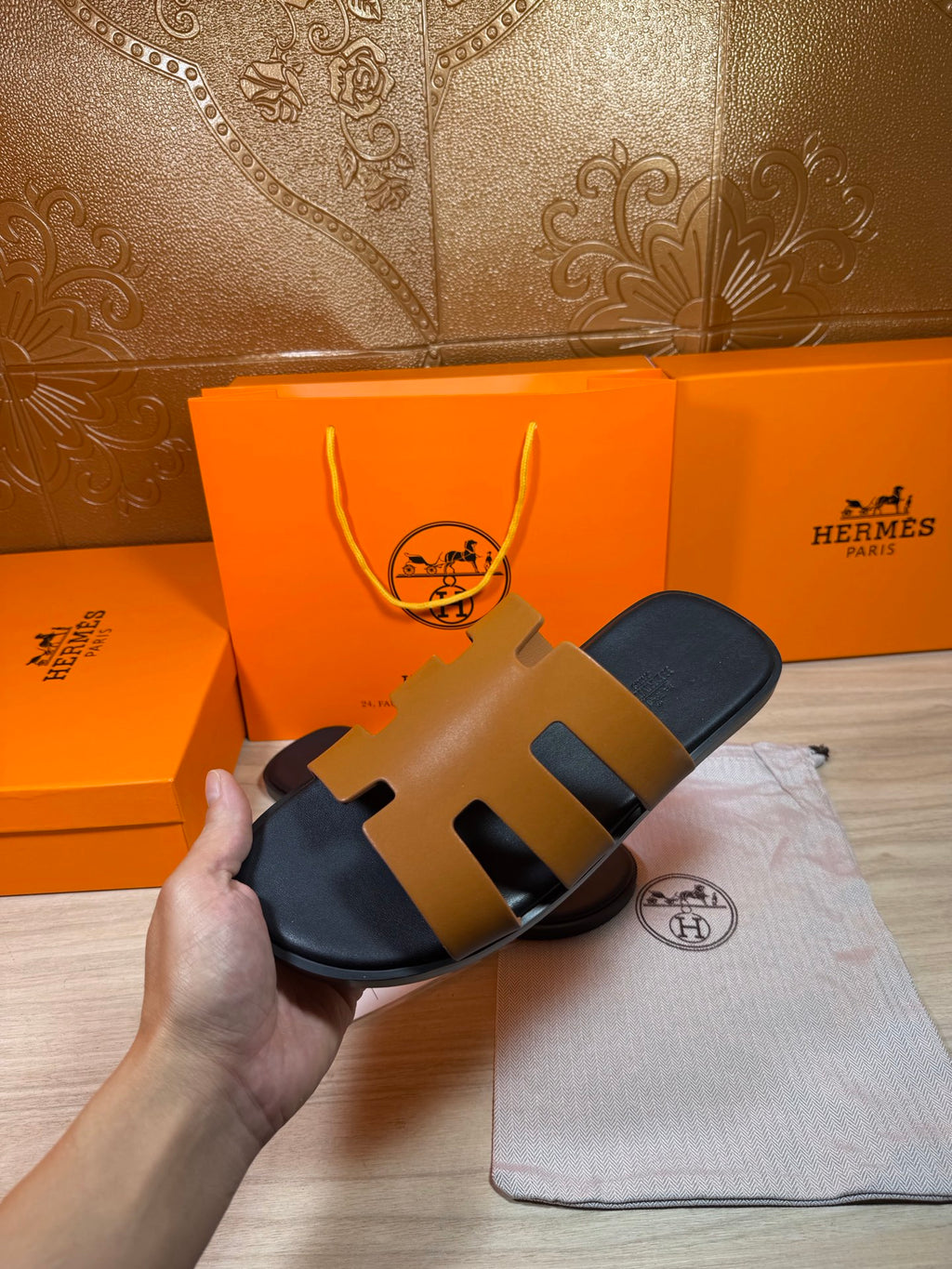 Hermes slide sandals on dust bag, tan straps with black footbed.