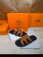 Hermes slide sandals with tan straps and black sole, shown with packaging accessories.