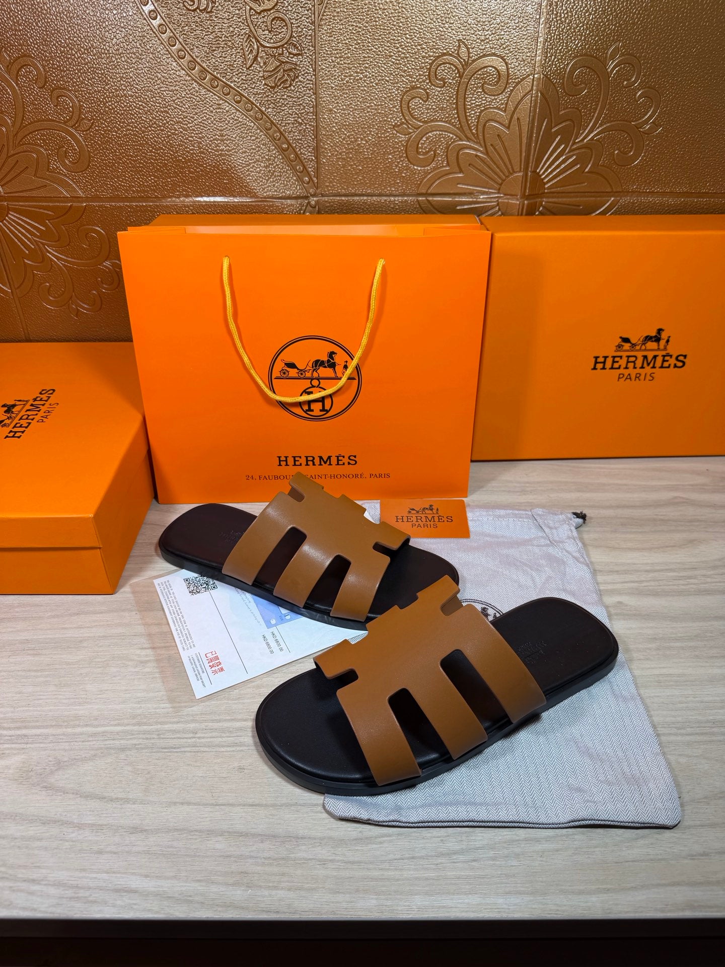 Hermes slide sandals with tan straps and black sole, shown with packaging accessories.