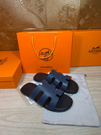 Hermes open-toe slide sandals, dark blue leather with three wide strap panels, front view.