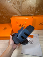 Hermes open-toe slide sandal, dark blue leather with three wide straps; held for display.