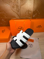 Hermes slide sandals with white straps over black footbed, front angle