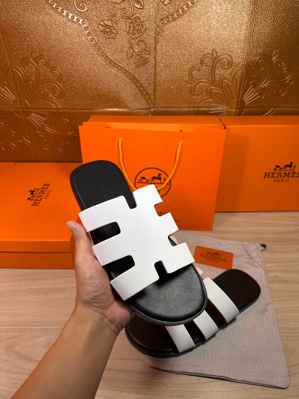 Hermes sandals with white straps on black base, held in hand