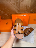 Hermes tan-brown slide sandal held up, wide cutout straps and flat sole