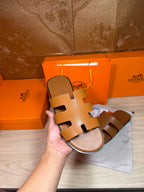 Hermes tan-brown leather slide sandal held in hand, openwork H straps