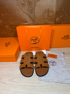 Hermes slide sandals with H-style cutout straps, tan-brown leather, flat sole
