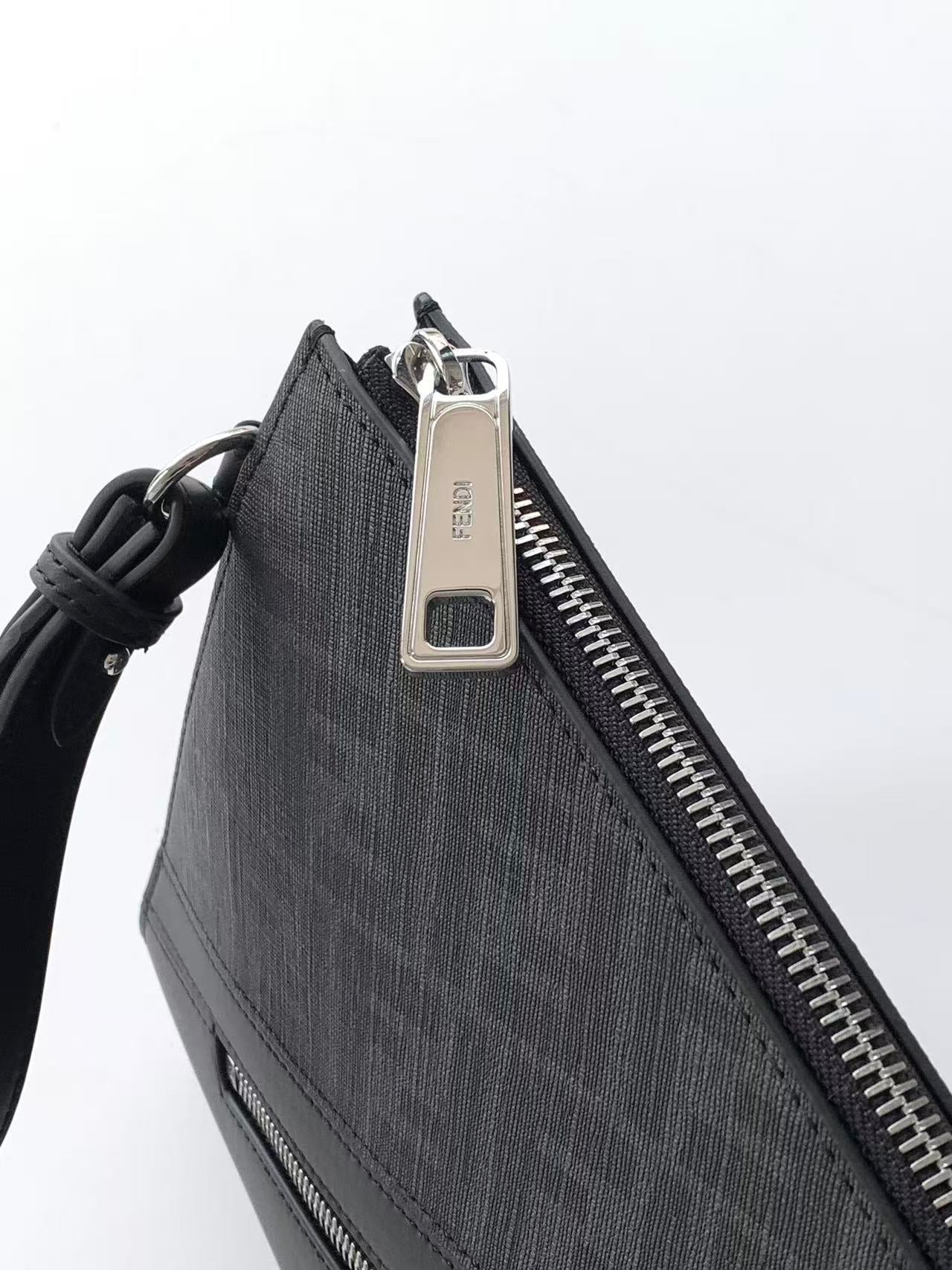 Fendi bag close-up of zipper pull and metal tag on dark textured fabric with leather trim.