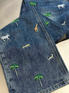 Blue denim pants laid flat with all-over palm tree and animal prints