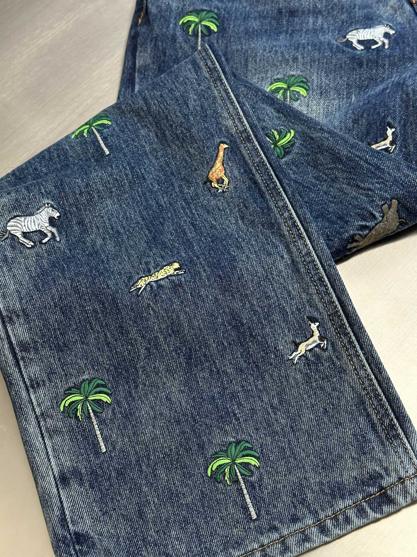 Blue denim pants laid flat with all-over palm tree and animal prints