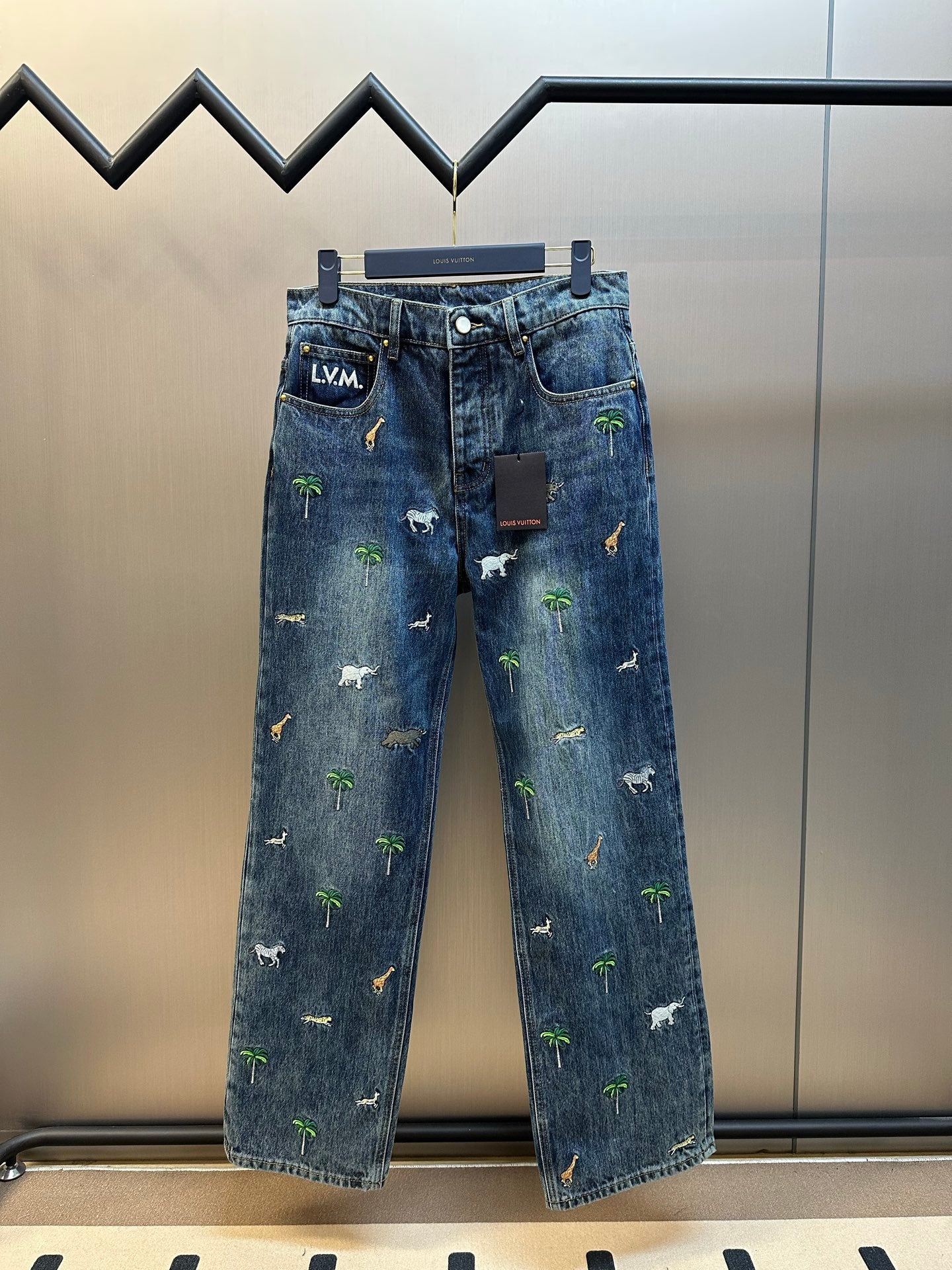 Blue denim pants with scattered animal and palm tree patches, front view