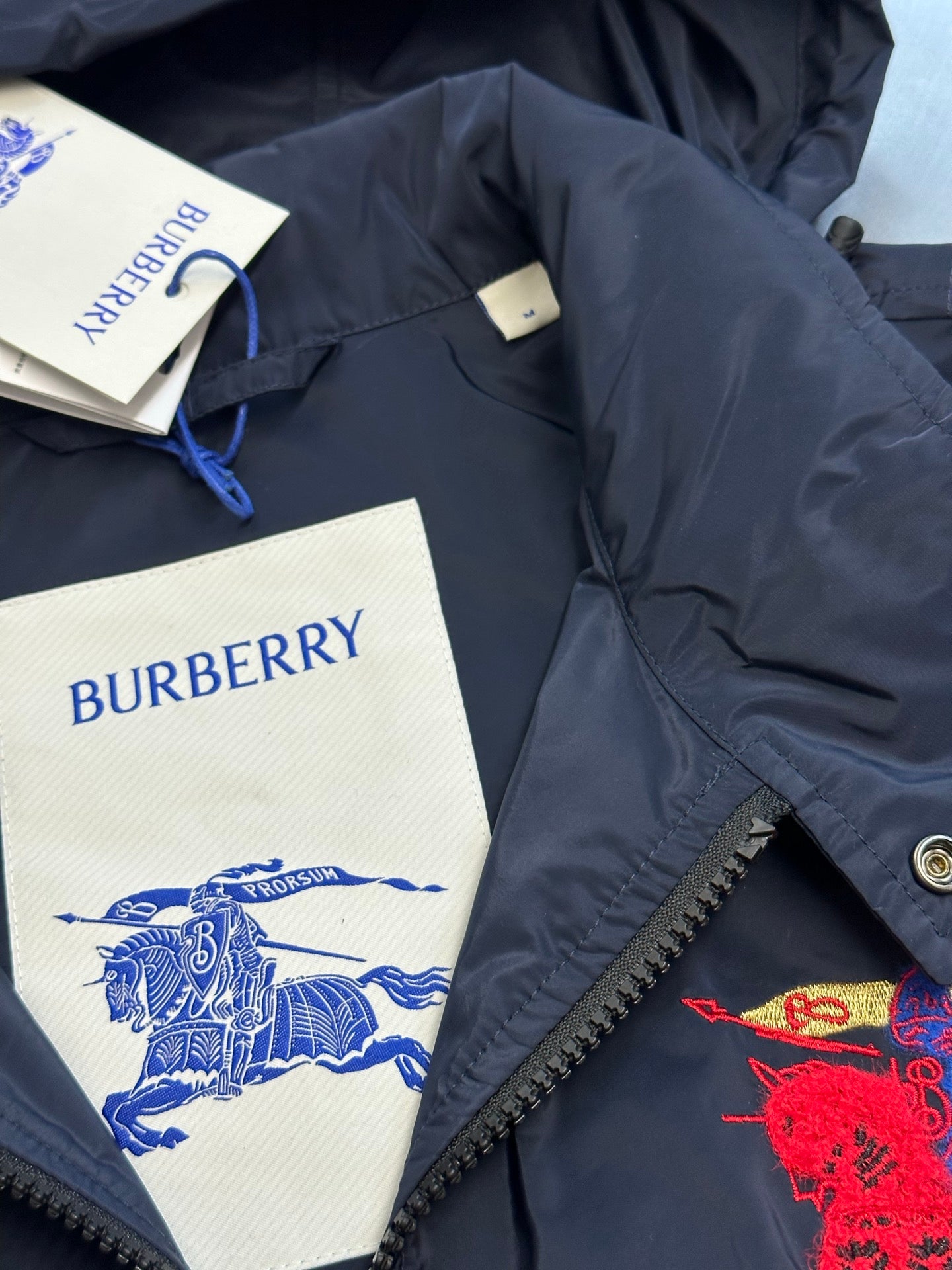 Navy jacket collar area with Burberry tags and red crest embroidery
