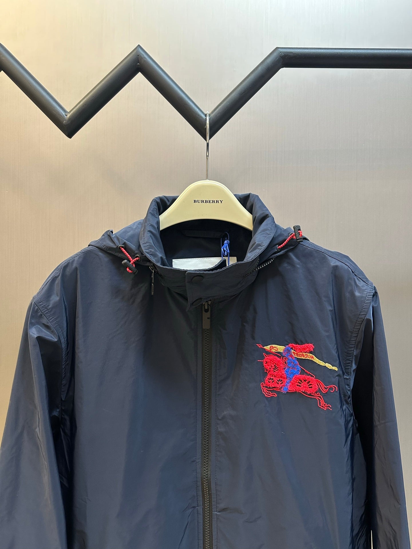 Navy hooded windbreaker jacket with red crest graphic on chest