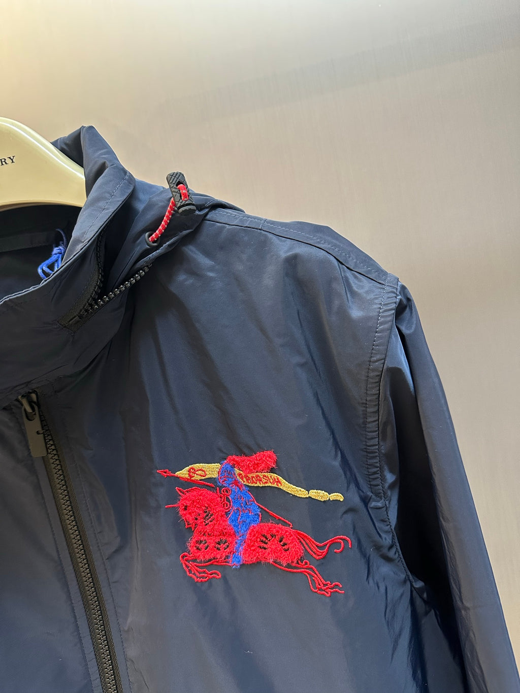 Navy zip-up jacket with red embroidered crest patch at upper chest