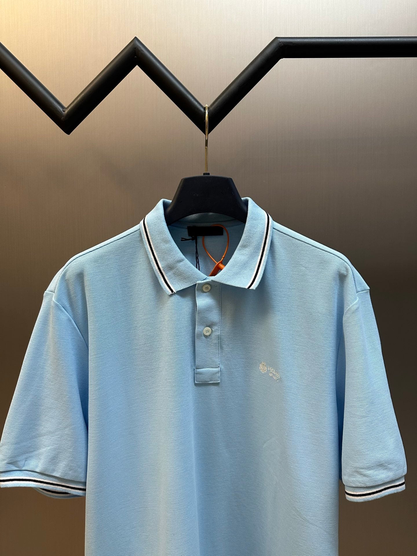 Prada light blue polo shirt with open collar and striped trim on cuffs