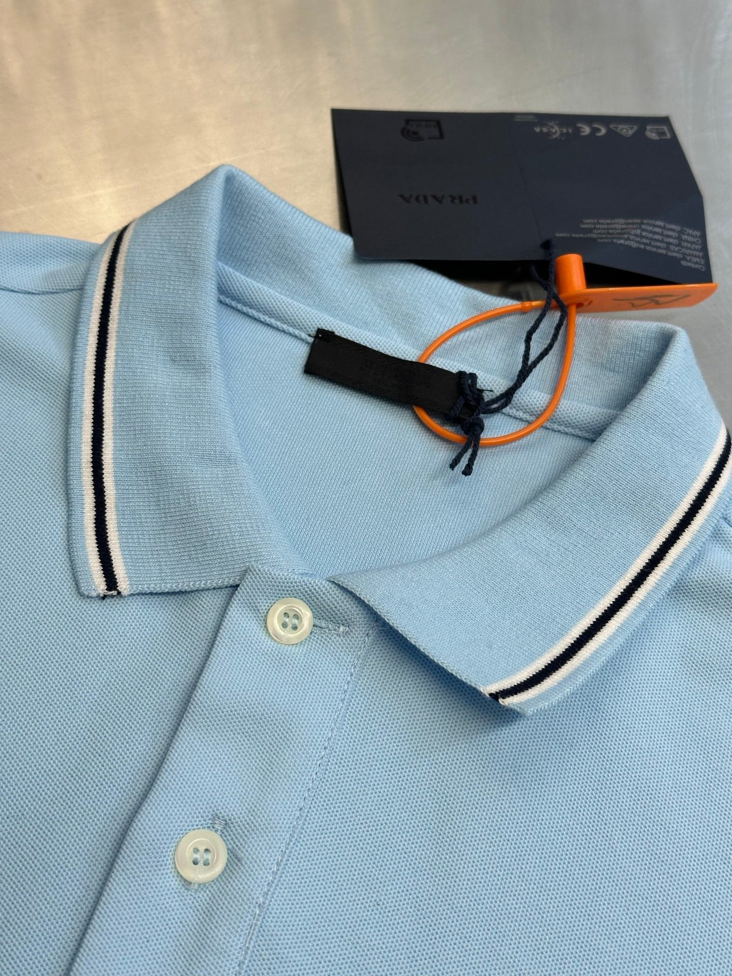 Prada light blue polo shirt neckline with buttons, striped trim, and hang tag