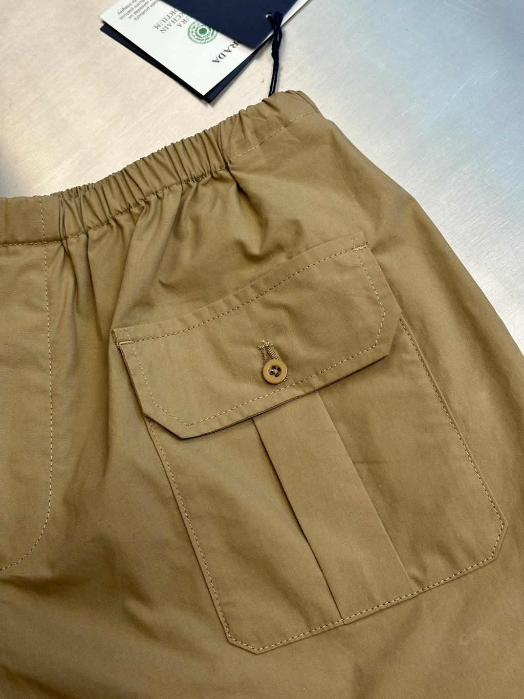 Beige cargo shorts with front patch pocket and round button closure.