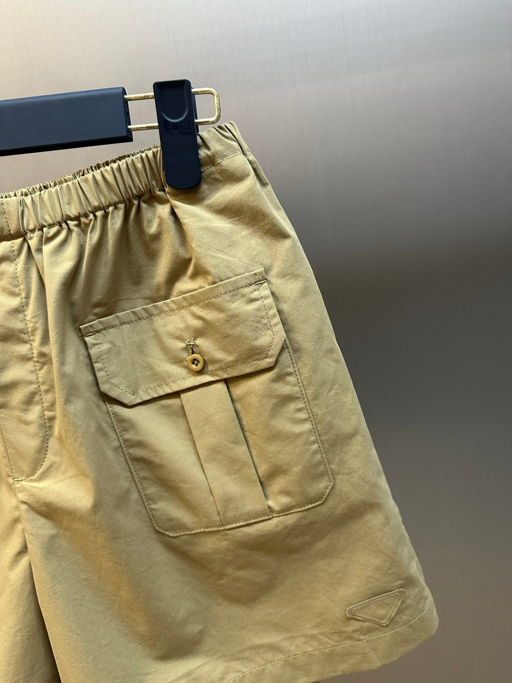 Beige cargo shorts front patch pocket with button and seam detail.