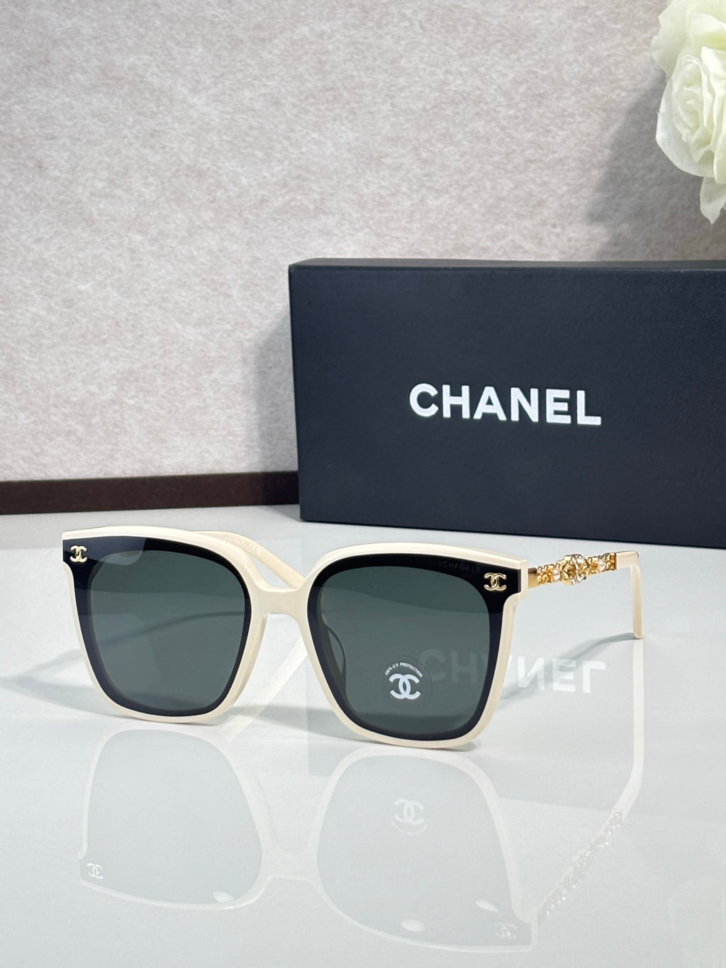 Chanel sunglasses with white frames, dark lenses, and gold chain-style temples