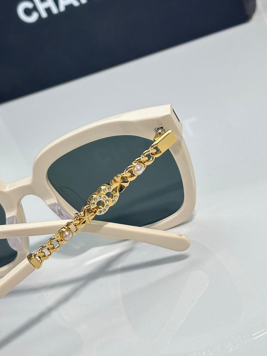 Chanel sunglasses close-up with white frame and gold chain pearl detail on arm